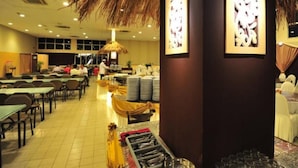 Un comedor amplio con varias mesas y sillas, una barra de buffet y un techo de paja.
