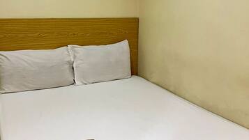 A single bed with a wooden headboard, white bedding, and a folded towel on the footboard.