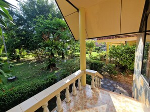 A balcony with a tiled floor and a railing, overlooking a garden with various trees and shrubs.