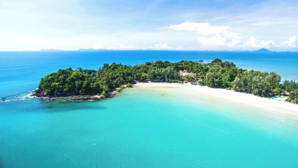 Eine Luftaufnahme einer tropischen Insel mit Strand, dichtem Grün und klarem türkisfarbenem Wasser.