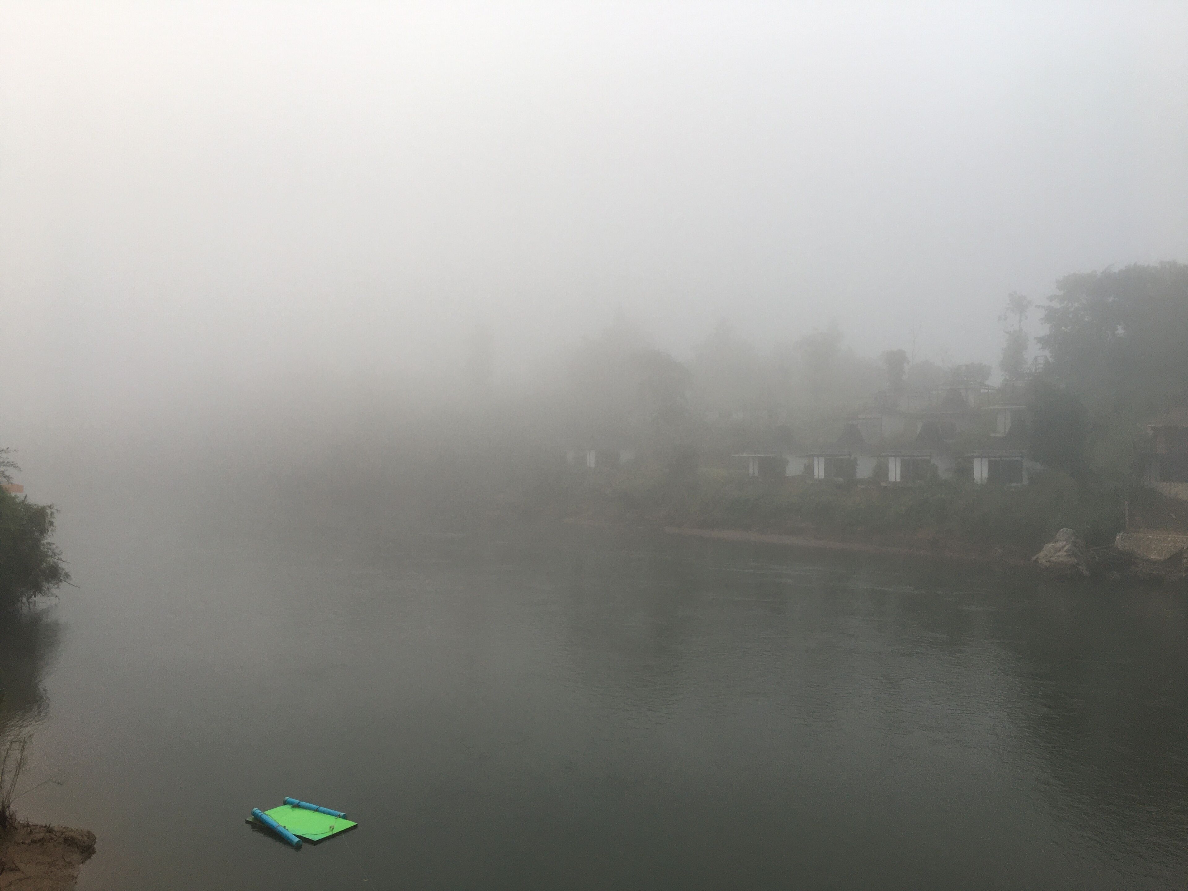 A foggy river scene with a small green boat.