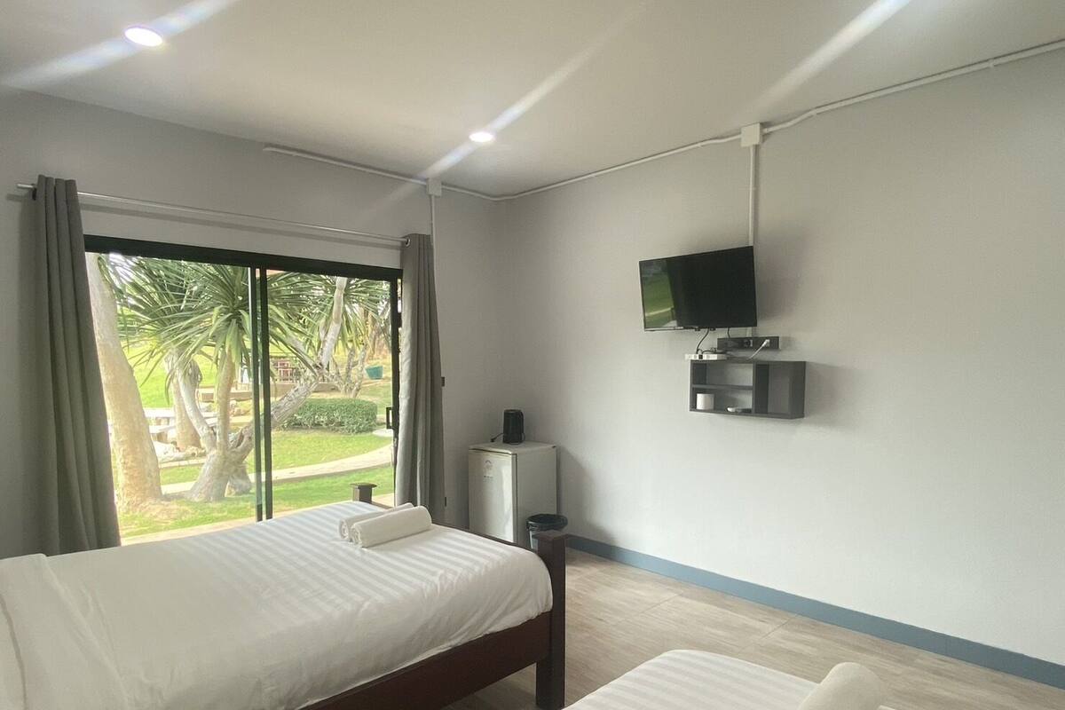 A hotel room with a bed, a TV mounted on the wall, and a view of a garden outside.