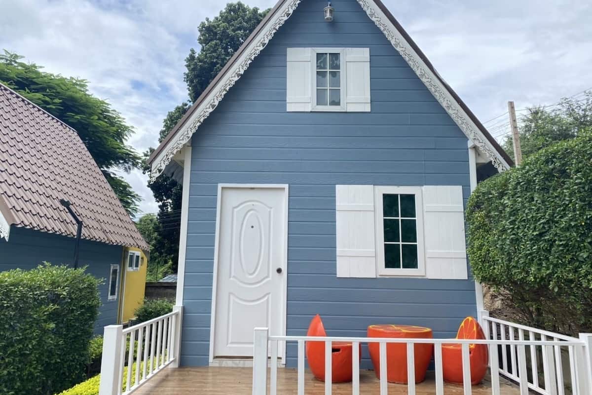 A blue house with a white door and window shutters, a small porch with orange chairs, and a white railing.