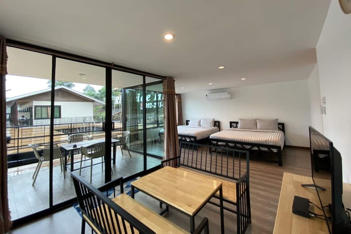 A modern room with a large sliding glass door leading to an outdoor area, two beds with striped bedding, a wooden table, and a TV on a wooden stand.