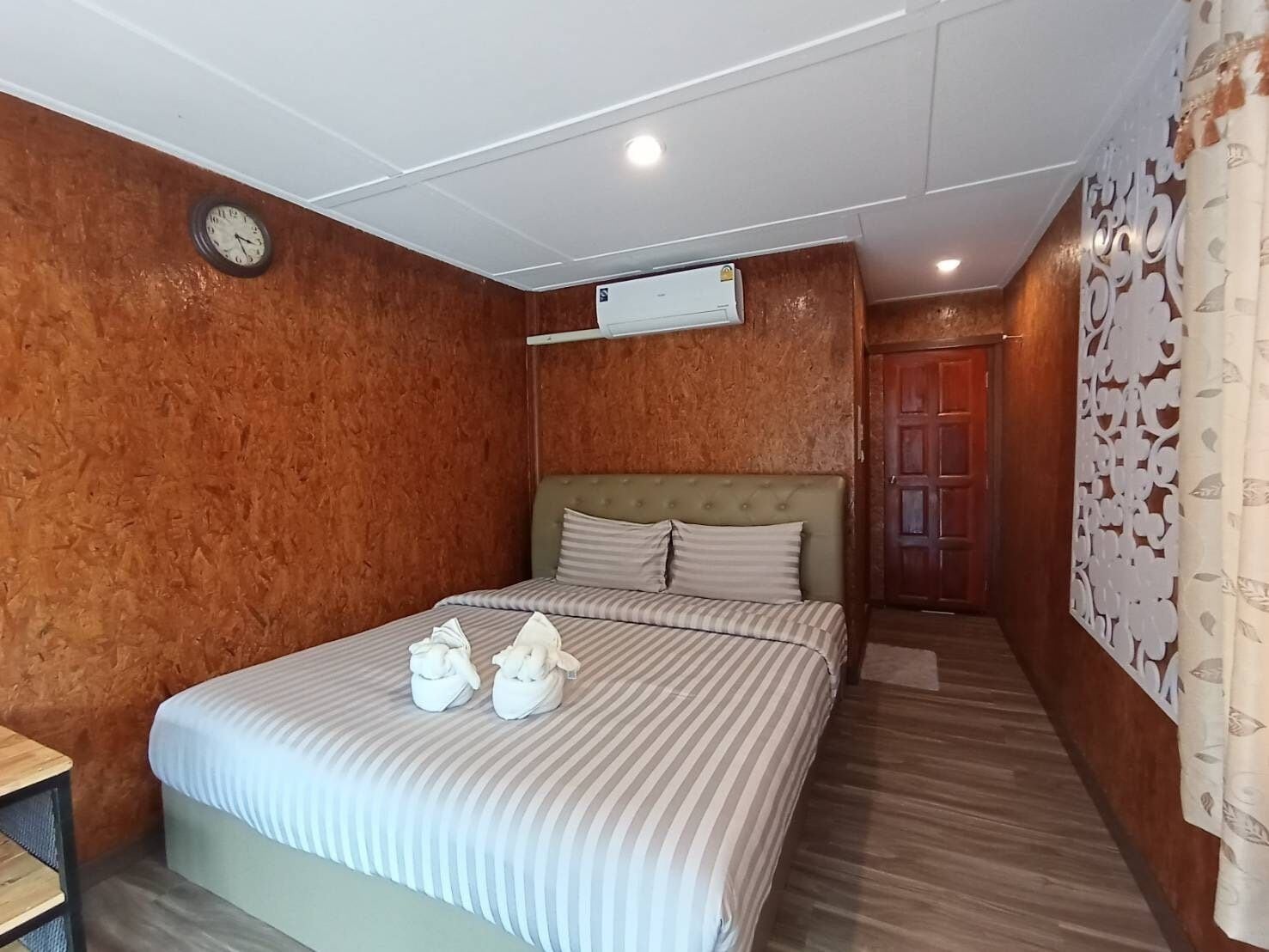 Ett hotellrum med en säng, en klocka, en luftkonditioneringsanläggning och en väggpanel av trä.