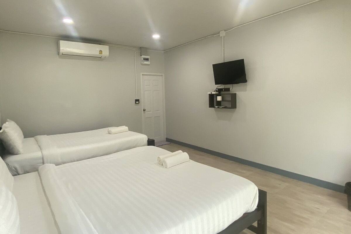 A hotel room with two beds, a TV, an air conditioning unit, and a door.