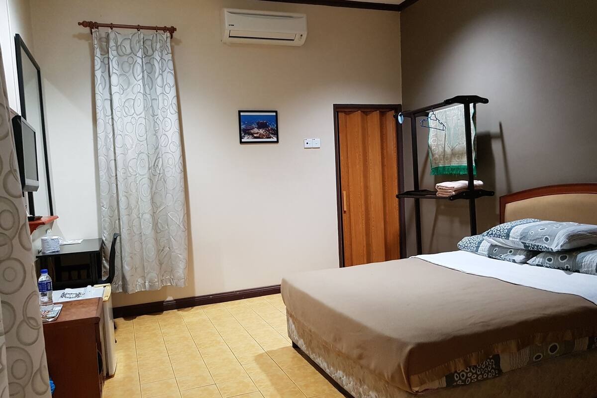 Ein Hotelzimmer mit Bett, Schreibtisch mit Stuhl, Kleiderschrank, Ablage mit Handtüchern und Klimaanlage.
