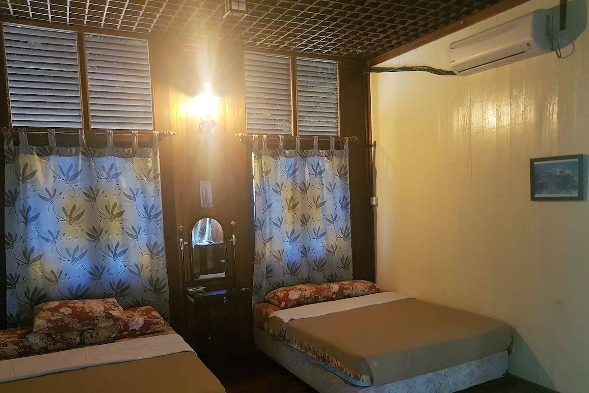Ein Zimmer mit zwei Einzelbetten, einem Spiegel, einer Tür und einer Klimaanlage.