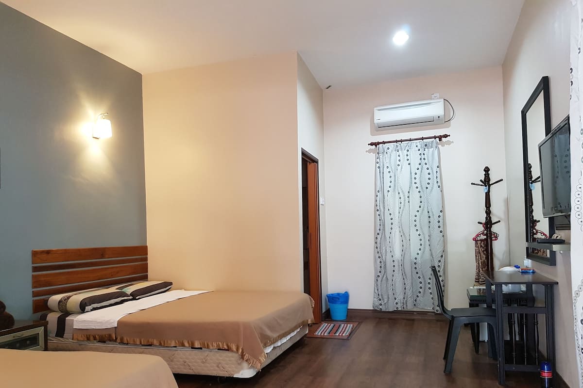 Ein Hotelzimmer mit zwei Betten, einem Schreibtisch, einem Stuhl, einer Klimaanlage und einem Vorhang mit Punkten.