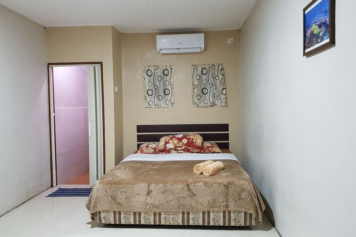 Ein Schlafzimmer mit einem Bett, einer Klimaanlage, gemusterten Vorhängen und einem gerahmten Bild an der Wand.