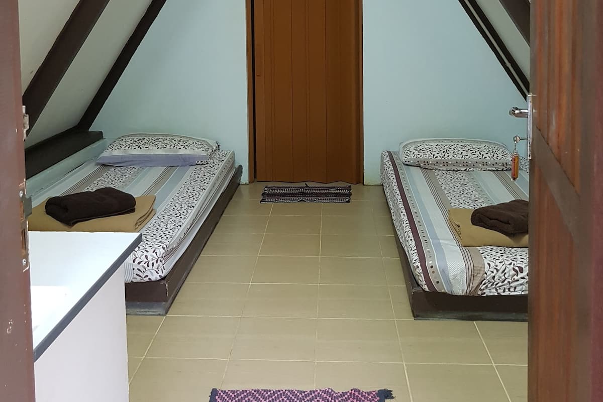 Ein kleines, dreieckiges Schlafzimmer im Dachgeschoss mit zwei Betten, einer Holztür und einer unter der Decke montierten Klimaanlage.