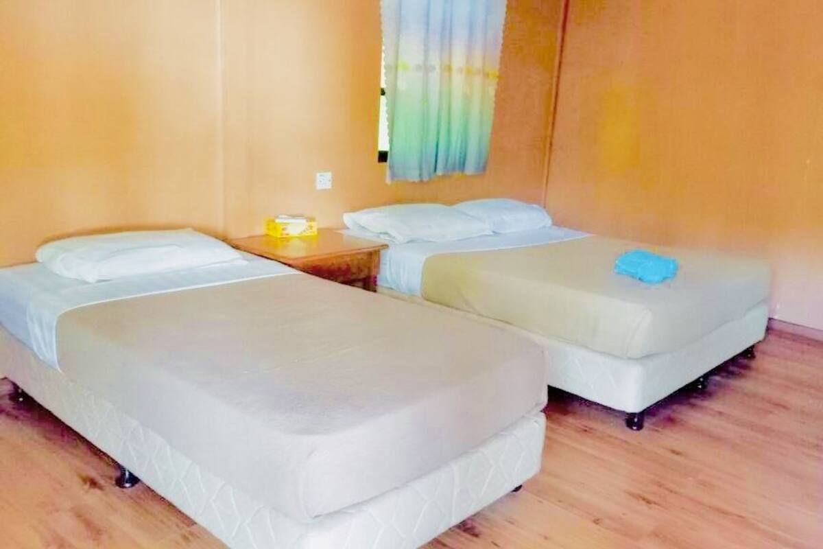 A room with two single beds, wooden flooring, and a curtain on the window.
