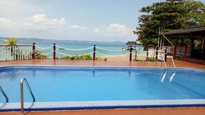 Piscina com vista para o mar, área cercada e zona de estar coberta.