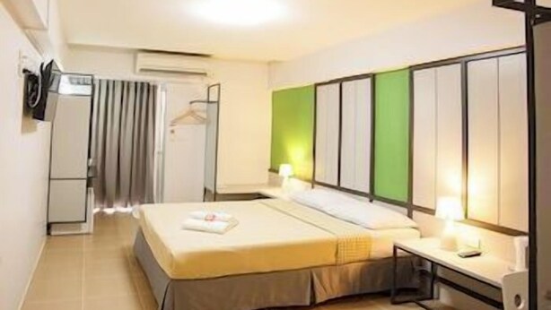 A hotel room with a bed, bedside table, and a green accent wall. - Regent Ngamwongwan (Nonthaburi)