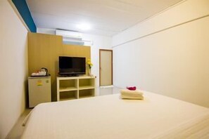 A hotel room with a bed, a television on a stand, a small refrigerator, and a door. - Regent Ngamwongwan (Nonthaburi)