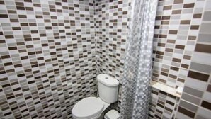A bathroom with a tiled floor and walls, a toilet, a trash bin, and a shower curtain. - Regent Ngamwongwan (Nonthaburi)