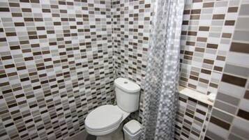 A bathroom with a tiled floor and walls, a toilet, a trash bin, and a shower curtain.
