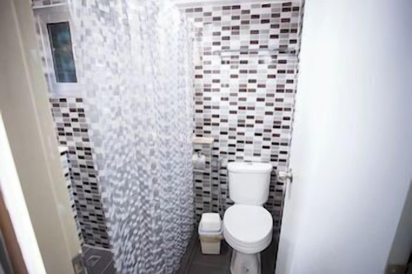 A bathroom with a tiled shower wall, a toilet, and a sink.