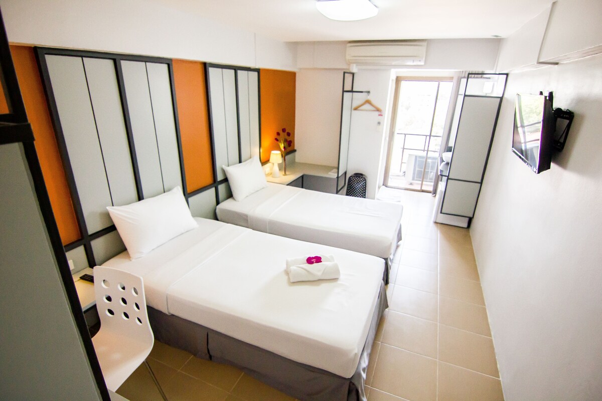 A hotel room with two beds, a chair, a desk, a mirror, and a window.