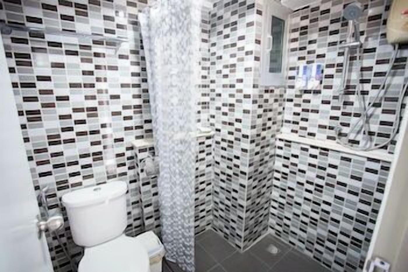 A bathroom with a toilet, a shower, and a tiled wall with a checkered pattern.