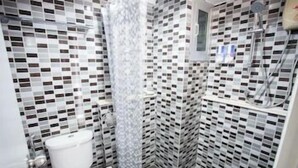 A bathroom with a toilet, a shower, and a tiled wall with a checkered pattern. - Regent Ngamwongwan (Nonthaburi)