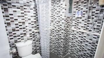 A bathroom with a toilet, a shower, and a tiled wall with a checkered pattern.