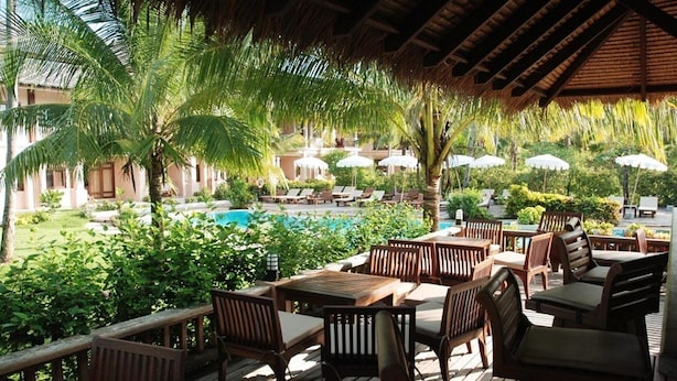 Un espacio al aire libre con mesas y sillas de madera, rodeado de exuberante vegetación y una piscina.