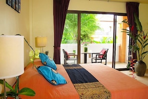 A hotel room with a bed, a lamp, a table, chairs, and a view of a garden through a sliding door.