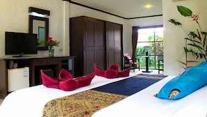 A hotel room with a bed, a TV, a desk with a computer, a wardrobe, and a window with a view of greenery. - Khaolak Palm Hill Resort (Takua Pa)