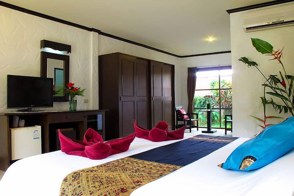 A hotel room with a bed, a TV, a desk with a computer, a wardrobe, and a window with a view of greenery.