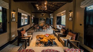 A spacious lobby with wooden furniture, a central coffee table, and large windows offering views. - Pugdundee Safaris - Ken River Lodge (Panna)