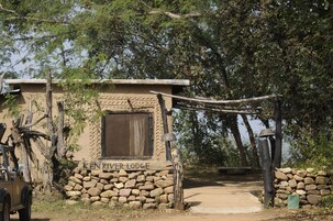 Entrada rústica a un albergue con un muro de piedra, un portón de madera y un letrero que dice "KEN RIVER LODGE".