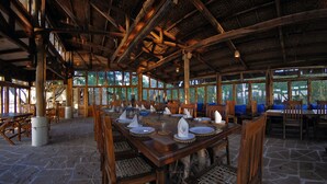 A spacious dining area with a high wooden ceiling and stone flooring, featuring a large table set for a meal. - Pugdundee Safaris - Ken River Lodge (Panna)