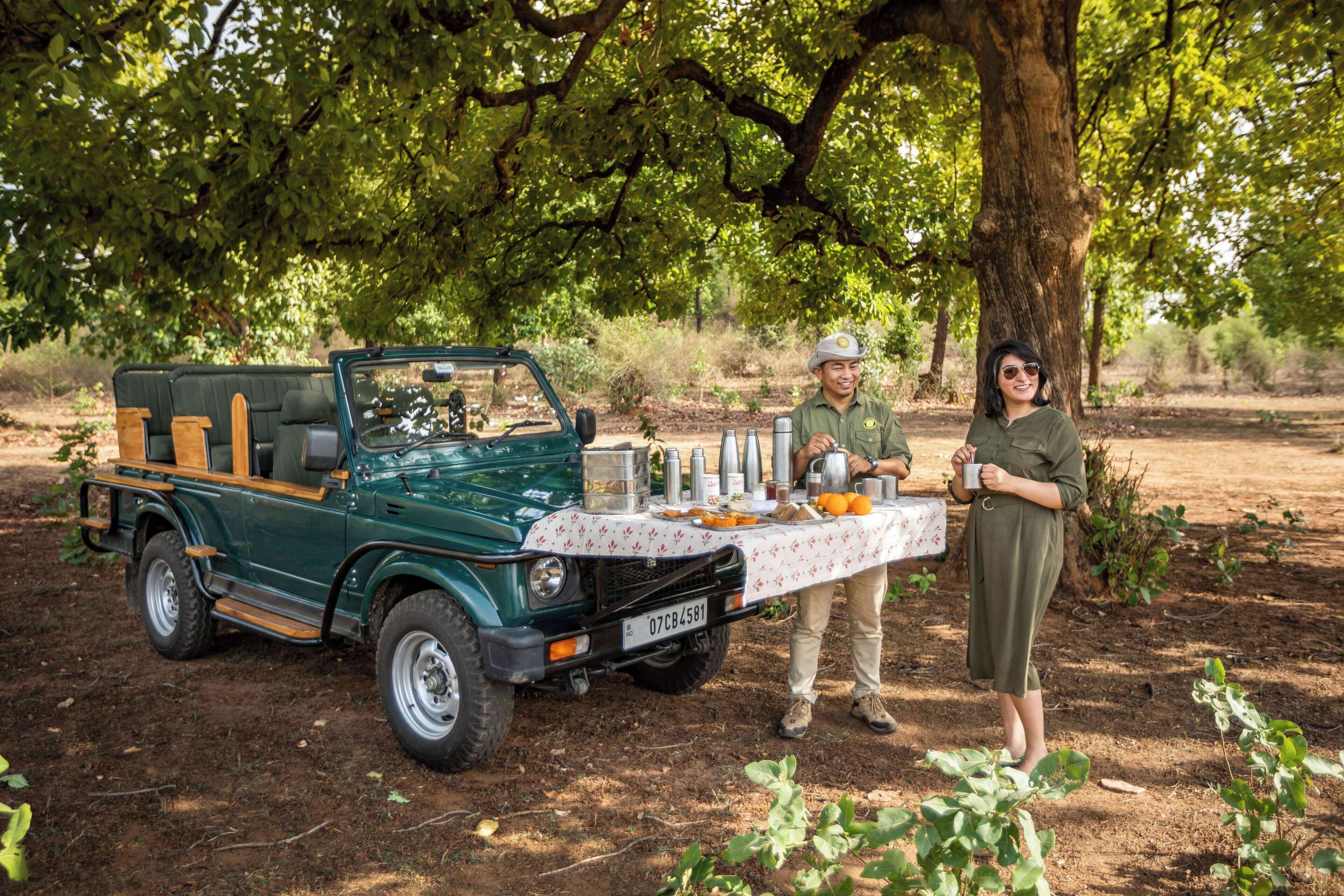 Un vehículo verde con una mesa instalada bajo un árbol, una persona con uniforme y otra vestida.