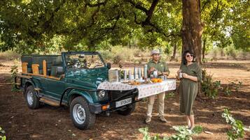 Un vehículo verde con una mesa instalada bajo un árbol, una persona con uniforme y otra vestida.