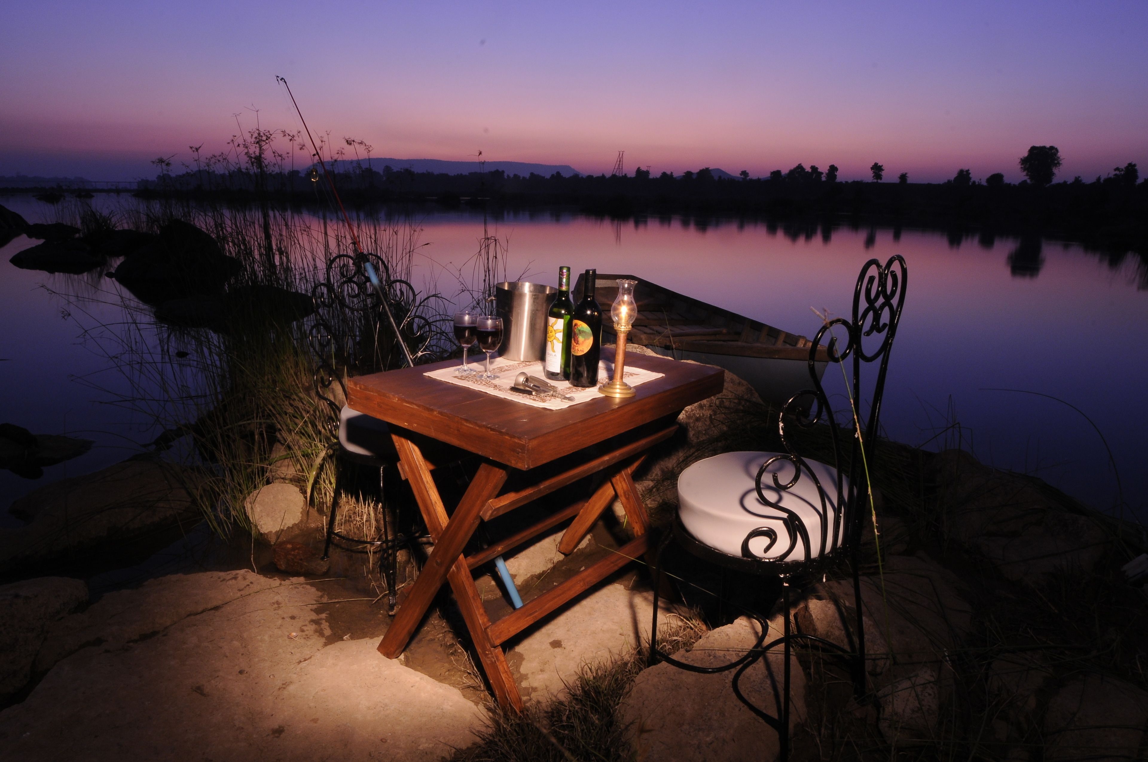Een houten tafel met een metalen stoel aan een meer bij zonsondergang.