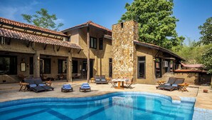 A swimming pool with lounge chairs and a stone pillar. - Pugdundee Safaris - Ken River Lodge (Panna)