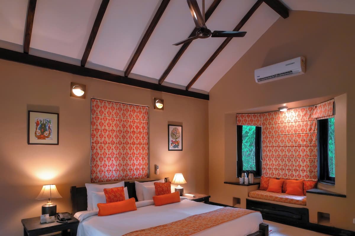 Een slaapkamer met een groot bed, twee nachtkastjes, een ventilator in het plafond, een airconditioning en een raam met gordijnen met een patroon.