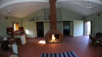 Un amplio salón con chimenea central, techos altos y un comedor con sillas y una mesa.