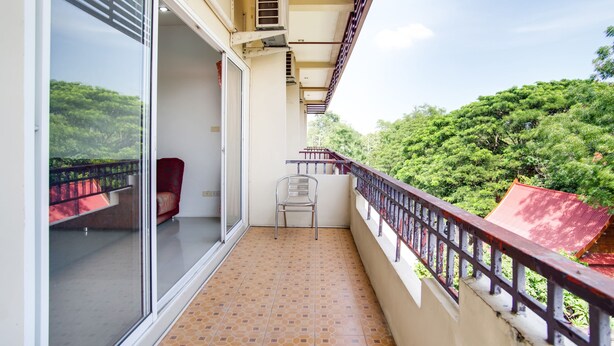 Ein Balkon mit Blick auf üppiges Grün, ein Stuhl und ein rotes Geländer.