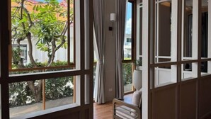 A room with large windows, a ceiling fan, and a view of trees and buildings outside. - Amphawa Nanon Hotel (Amphawa)