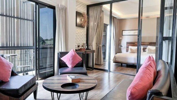 A modern hotel room with a balcony, a bed, a seating area with a table, and a view through large glass doors. - Amphawa Nanon Hotel (Amphawa)