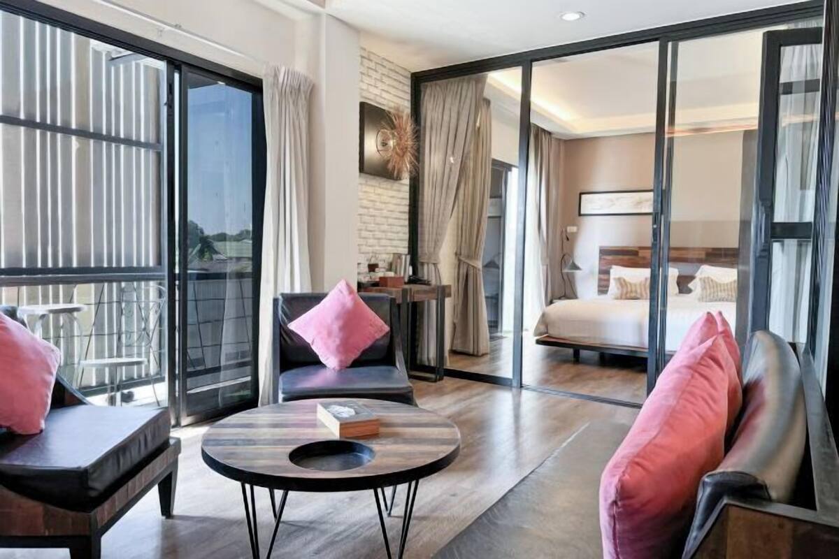 A modern hotel room with a balcony, a bed, a seating area with a table, and a view through large glass doors.