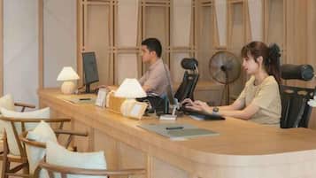 A reception desk with two staff members, a fan, and a lamp.