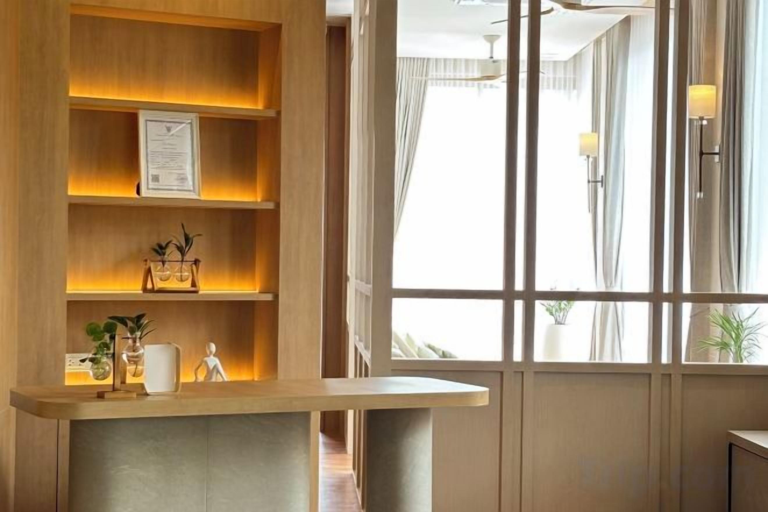 A reception desk with a wooden finish, a framed certificate, and a small plant. There is a window with curtains and a view of the outside.