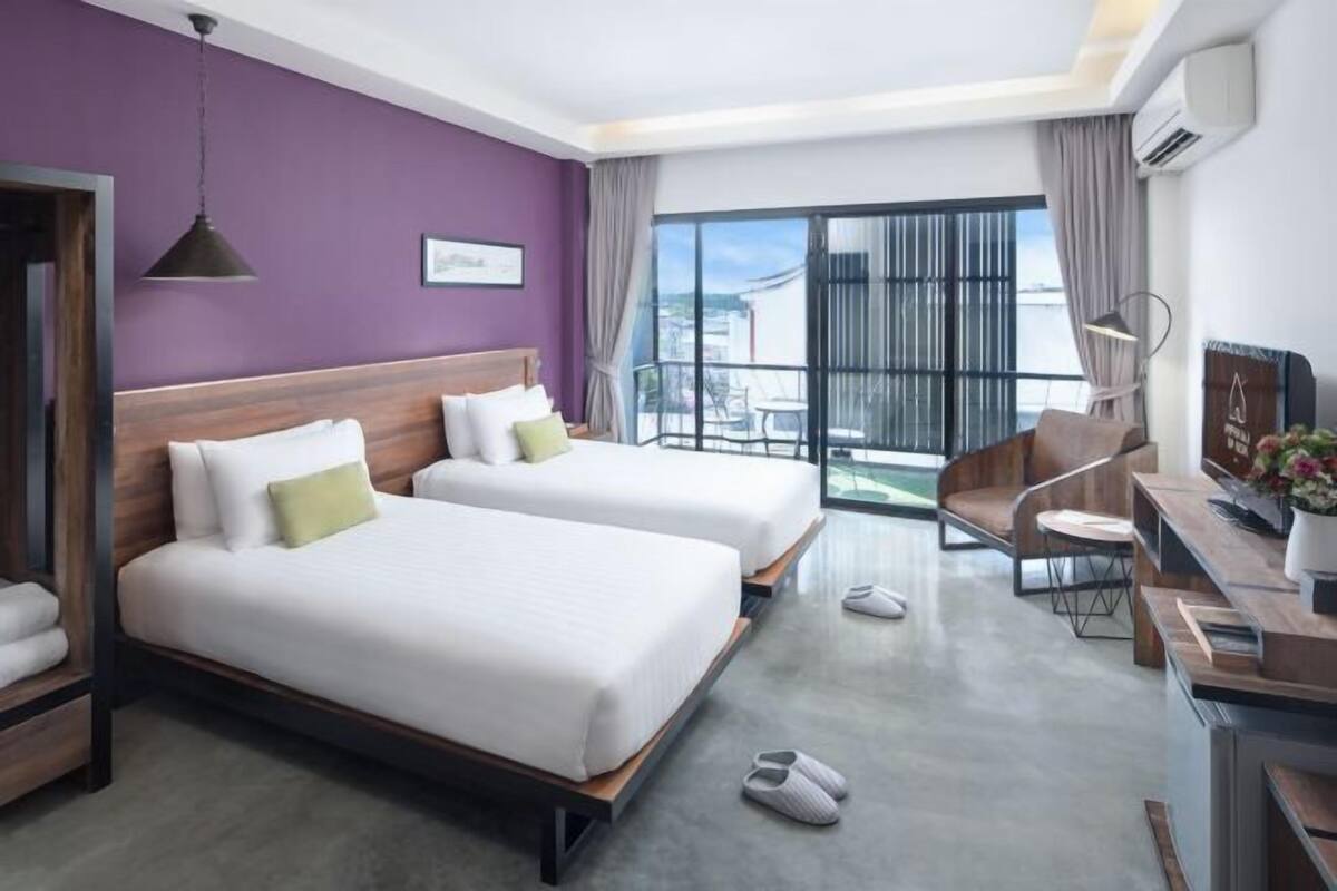 A hotel room with two beds, a desk, a chair, and a balcony with a view.