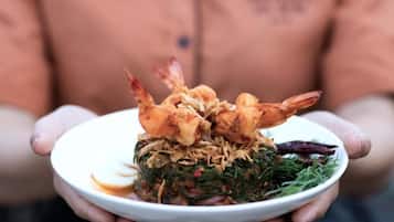 A person holding a plate with a dish containing shrimp and greens.