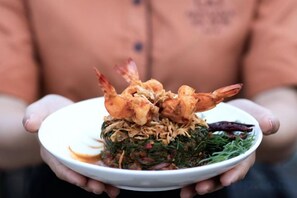 A person holding a plate with a dish containing shrimp and greens. - Amphawa Nanon Hotel (Amphawa)