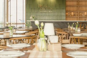 A restaurant interior with tables set for dining, a green wall with the name 'Lana Non' and 'EATERY & BAR' signage, and a wooden panel wall with decorative elements. - Amphawa Nanon Hotel (Amphawa)