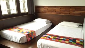 Two single beds with white linens and colorful quilts, a wooden headboard, and a window with blinds. - At One (Bangkok)